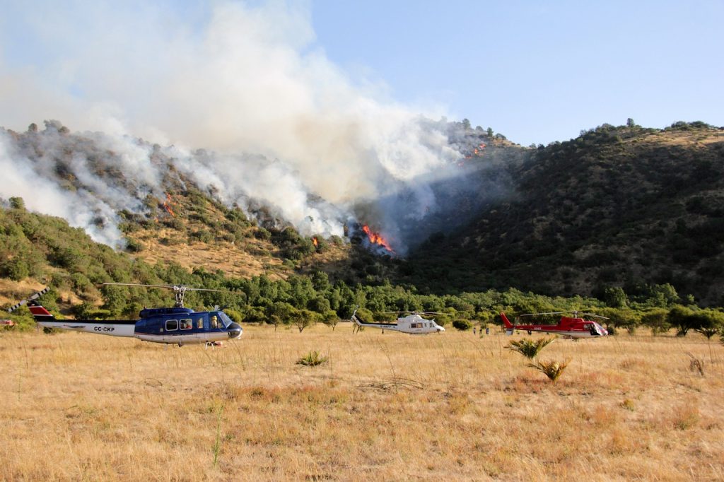 helicopters fly near a forest fire