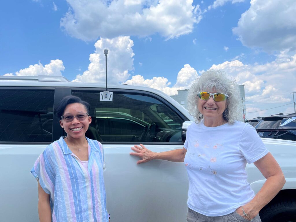 Two women stand next to a car equipped with a heat sensor at the urban heat island mapping campaign.