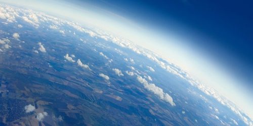 Aerial view of earth with land and clouds visible in the left lower side of image, dark blue space in upper right