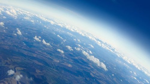 Aerial view of earth with land and clouds visible in the left lower side of image, dark blue space in upper right