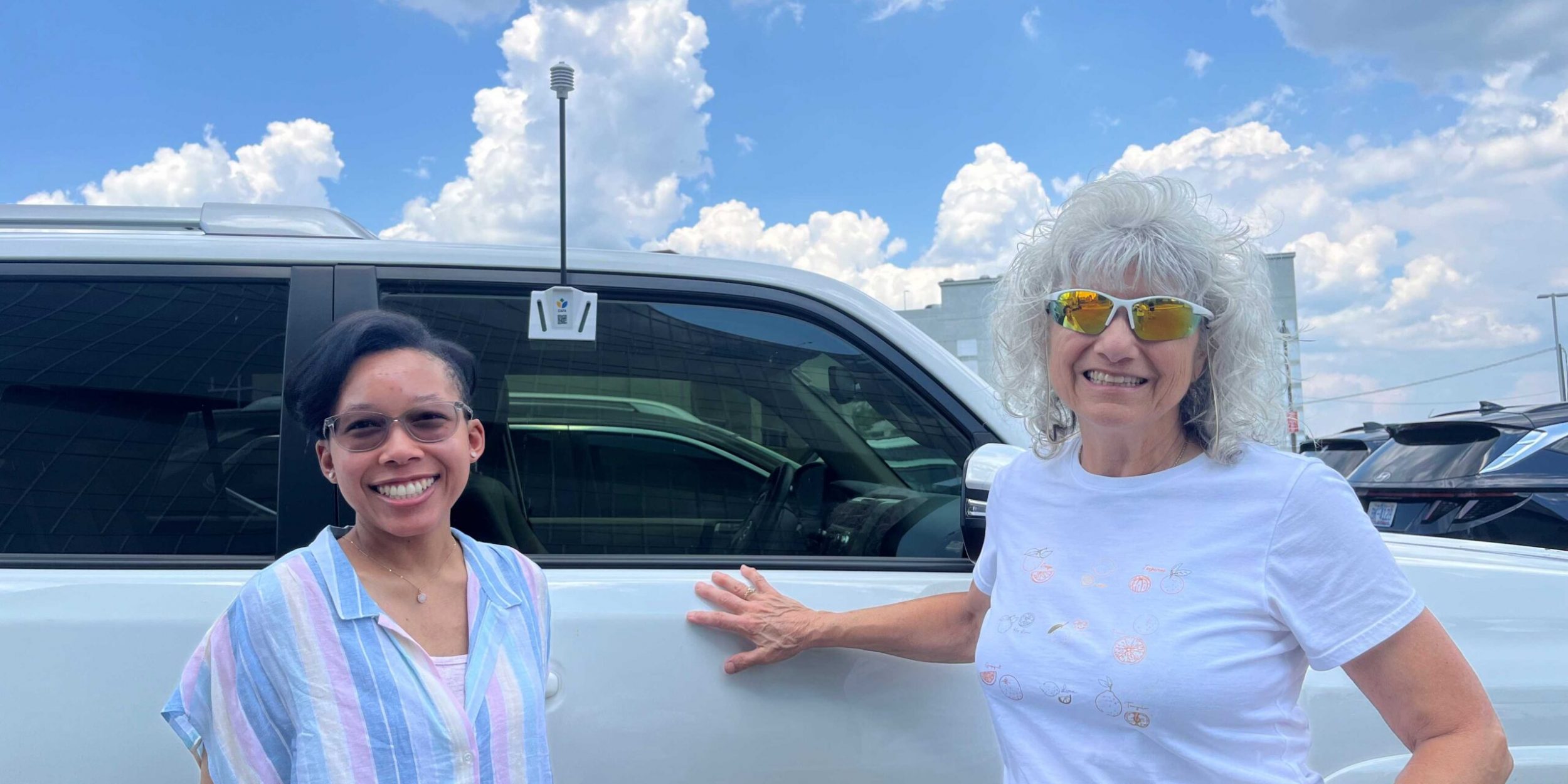 Two women stand next to a car equipped with a heat sensor at the urban heat island mapping campaign.