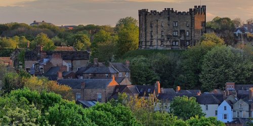 Distant view of stone buildings interspersed with trees against a yellow sky