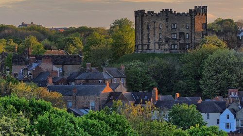 Distant view of stone buildings interspersed with trees against a yellow sky