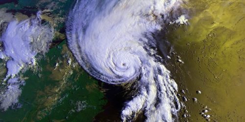 Aerial view of a hurricane. White clouds over yellow, green, and blue surface.