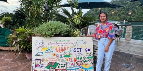woman poses next to a hand-drawn sign for the workshop in Palau